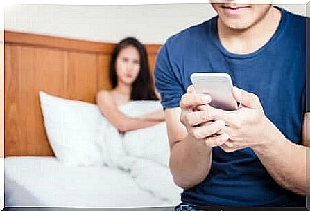 Couple relationship: woman looks from bed at her partner with cell phone