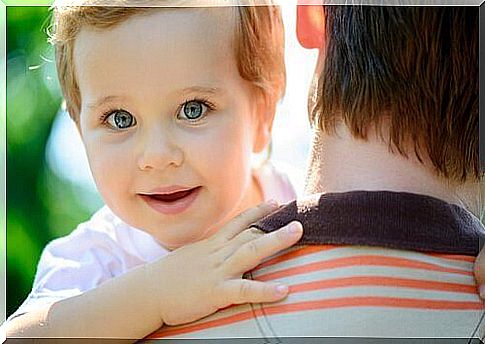 A father holds his child in his arms, who is looking at the camera.